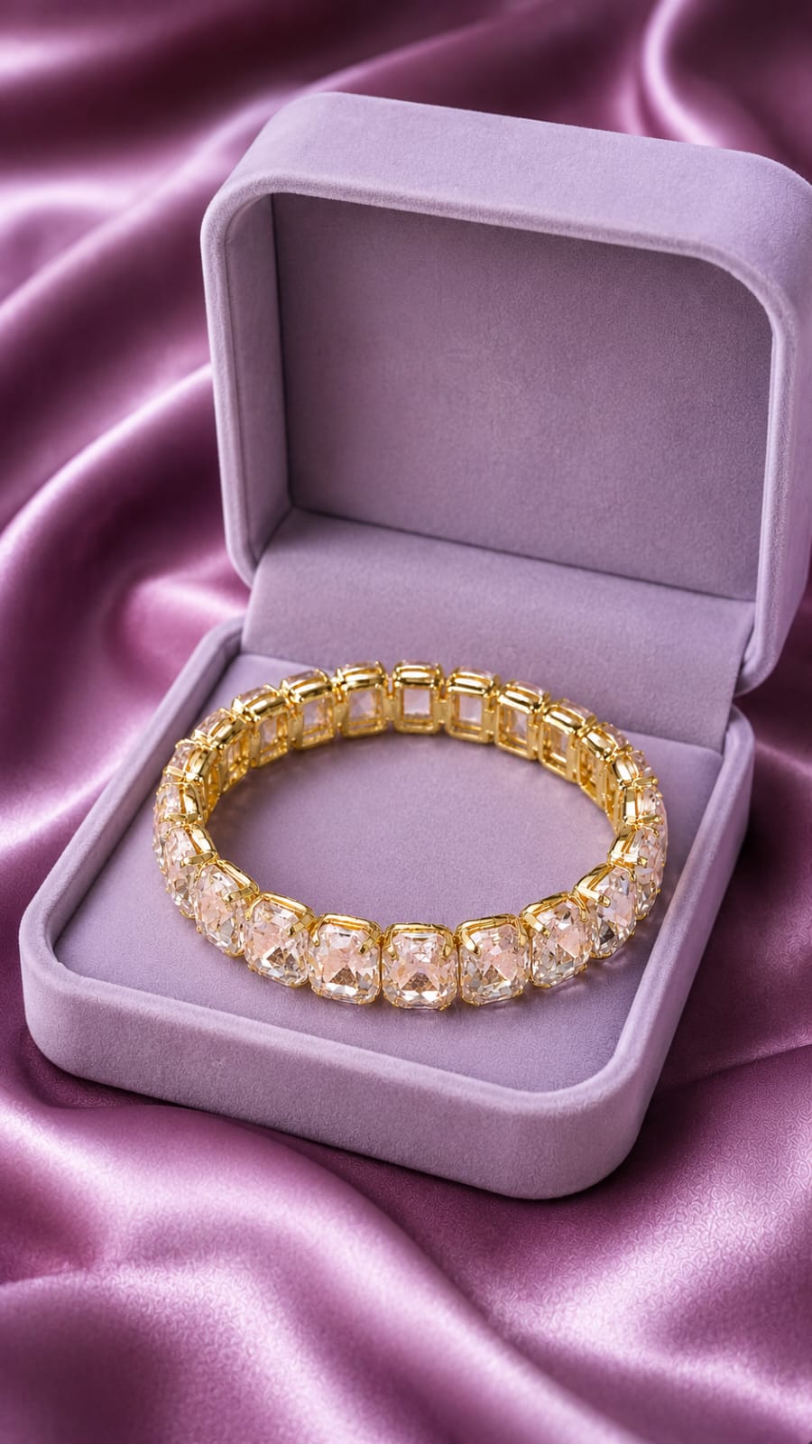 Gold-tone tennis bracelet with clear oval crystals, resting in a light purple gift box.