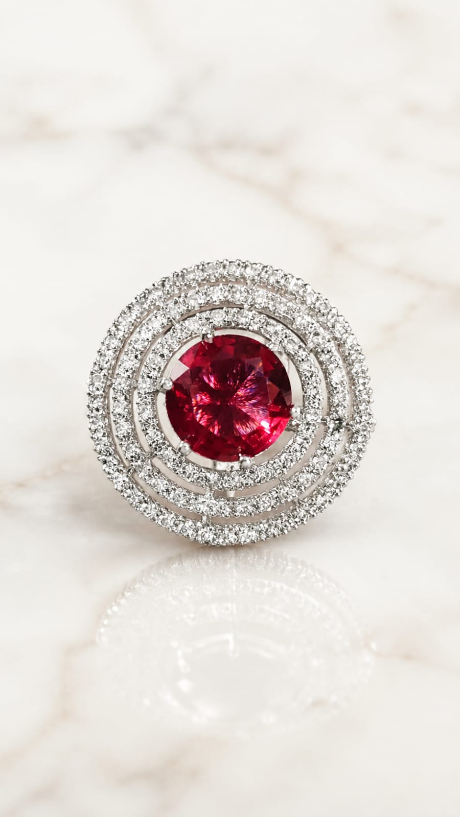 Silver-toned round red gemstone halo ring on light marble surface, front view