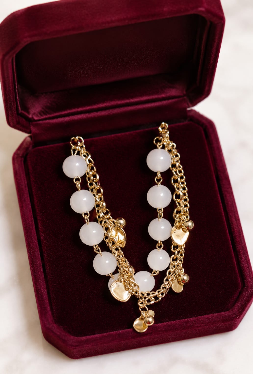 Gold-plated charm bracelet with white round beads and dangling gold charms