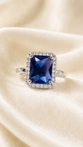 Silver ring with large sapphire-blue square center and sparkling halo around it