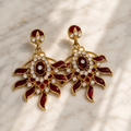 Gold-tone drop earrings: red enamel petals, round dark stones, white rhinestones.