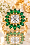 Gold statement ring with emerald-green petals and central clear square crystal, reflective
