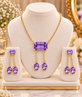 Gold pendant necklace with purple rectangular stone and matching oval drop earrings on display