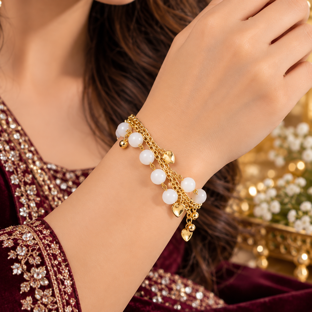 Gold-plated charm bracelet with white pearl beads and dangling heart charm on wrist