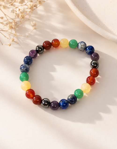 Seven chakra bracelet on white surface, multicolor beads with silver-toned round links